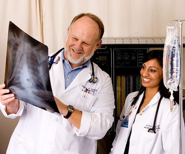 Male and female doctors wearing white lab coats and examining an x-ray.