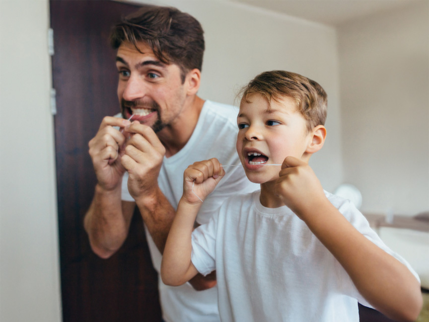 Father and son flossing together in front of a mirror, promoting family oral health and good hygiene habits in the Master of Public Health program.