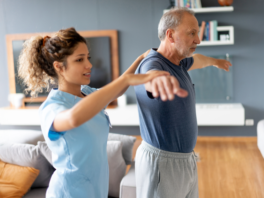 Masters in Kinesiology student assisting an elderly man with an arm exercise, highlighting the patient-centered approach of the program.